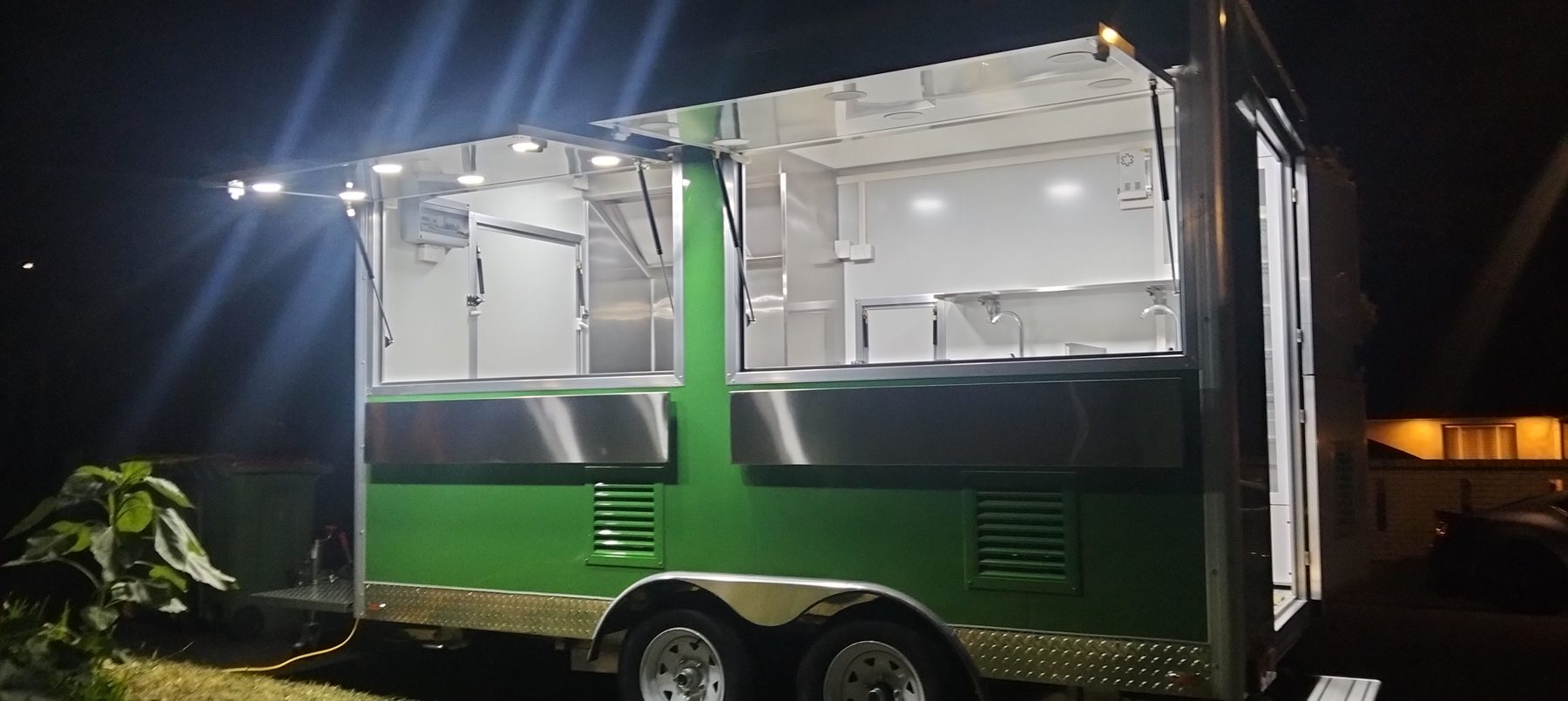 Green full-size food trailer lit up at night with two serving windows
